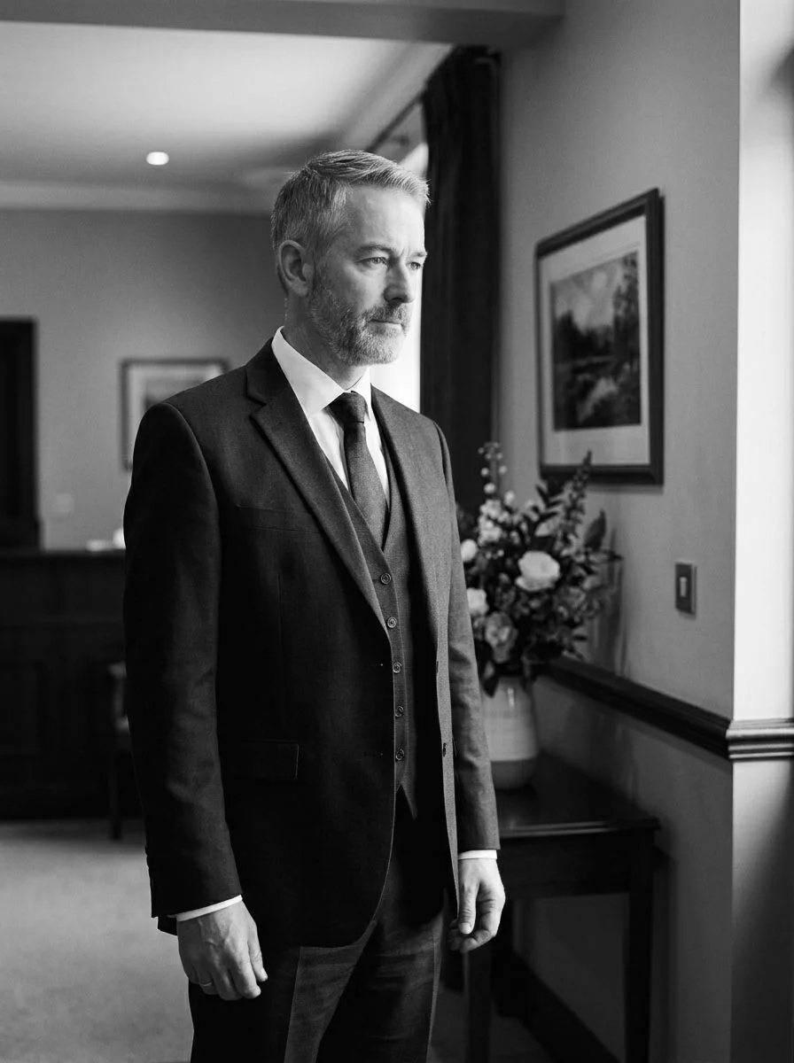 An independent funeral director standing calmly at the entrance of their funeral home, professional and approachable, warm natural light.